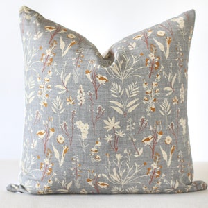 May include: Square throw pillow with a gray background and a floral pattern in cream, rust, and brown. The pillow features a botanical design with various leaves and flower shapes, creating a natural aesthetic.