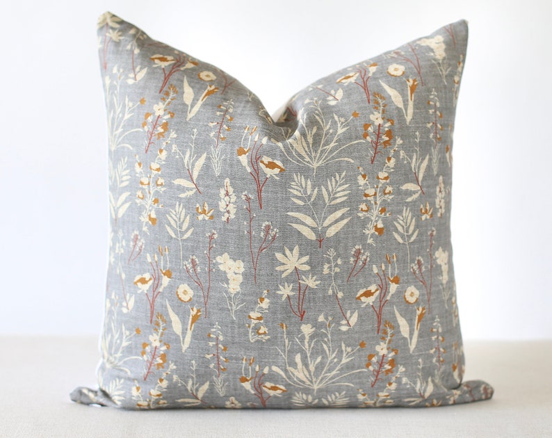 May include: Square throw pillow with a gray background and a floral pattern in cream, rust, and brown. The pillow features a botanical design with various leaves and flower shapes, creating a natural aesthetic.