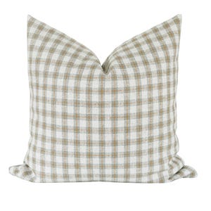 May include: Square throw pillow with a classic gingham pattern in white and tan. The pillow has a soft, textured appearance and is designed for decorative use on a bed or sofa. The pillow is a neutral color and will complement any decor.