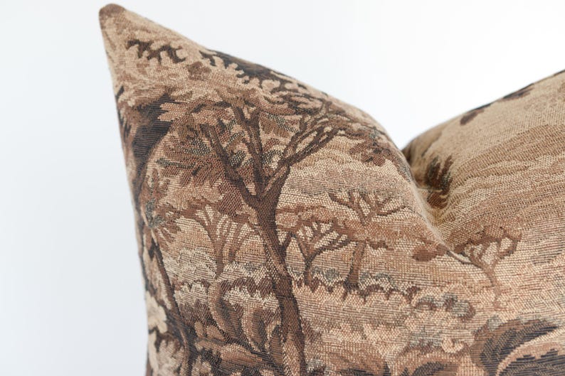 Puede incluir: Un coj&iacute;n cuadrado con un dise&ntilde;o de tapiz tejido en tonos marr&oacute;n, beige y bronceado. La tela muestra un patr&oacute;n de paisaje detallado con representaciones de &aacute;rboles y follaje en toda la superficie de la funda del coj&iacute;n.