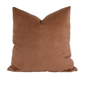 May include: A square, solid-colored pillow in a warm, earthy brown hue. The pillow has a soft, velvety texture and a classic, inviting design. Perfect for adding a touch of comfort and style to any living space.