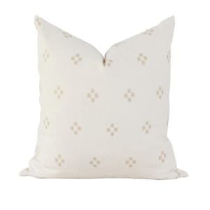 May include: A square throw pillow in an off-white cream color featuring a repeating pattern of small, light beige geometric cross shapes distributed evenly across the front surface of the fabric cover, creating a subtle and uniform textured appearance.
