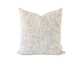 May include: A square throw pillow featuring a textured, woven fabric in a neutral color palette. The surface displays a complex, multi-tonal pattern of cream, beige, light gray, and soft brown threads interlaced to create a dense, tactile appearance.
