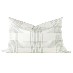 May include: A rectangular throw pillow featuring a white base color with a subtle, thin-lined plaid pattern in a muted sage green. The design consists of intersecting vertical and horizontal lines forming a grid across the entire surface.