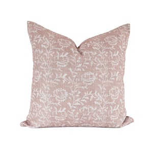 May include: A square throw pillow featuring a dusty rose pink base color with a repeating white floral and vine pattern printed across the fabric. The pillow has a soft, textured appearance with a visible weave and a classic knife-edge finish.