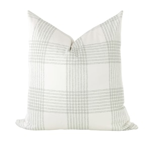 May include: A square throw pillow featuring a white base fabric with a subtle grey plaid pattern. The design consists of thin, intersecting grey lines forming a grid across the surface, creating a clean and structured appearance on the pillow cover.