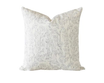 May include: A square throw pillow featuring an off-white base color with a repeating line-art pattern of grey poppies, stems, and leaves. The pillow has a soft, plump appearance with a subtle indentation at the top center of the fabric cover.