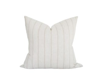 May include: A square throw pillow featuring a light cream or off-white base color with thin, vertical, light gray pinstripes running from the top to the bottom edge. The pillow has a soft, textured fabric appearance and a classic square shape.