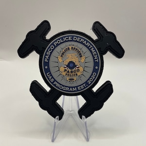 May include: A black and gray patch with the text "PASCO POLICE DEPARTMENT UAS PROGRAM EST. 2020" around a silver badge with the text "PASCO POLICE" and a stylized image of a drone.