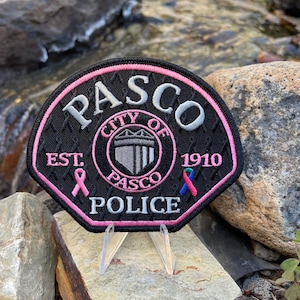 Peut inclure: Un écusson brodé noir et rose avec les mots "PASCO CITY OF EST. 1910 POLICE" et un sceau de la ville. L'écusson présente un ruban rose et un ruban bleu et rose.