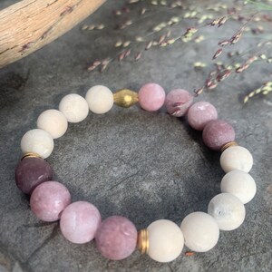 May include: A bracelet made of white and pink beads with gold accents. The bracelet is made of natural stones and is a beautiful and unique piece of jewelry.