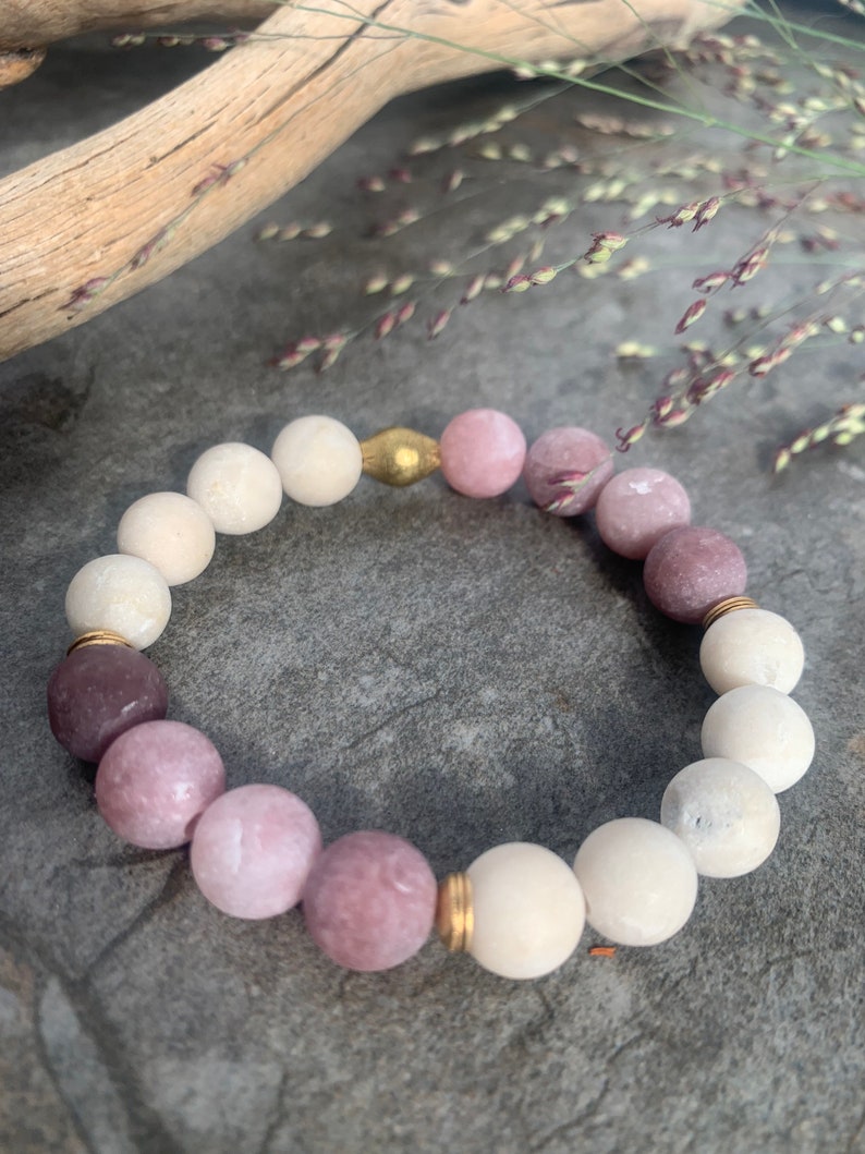 May include: A bracelet made of white and pink beads with gold accents. The bracelet is made of natural stones and is a beautiful and unique piece of jewelry.