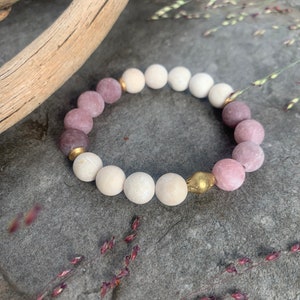 May include: A bracelet made of pink and white beads with gold accents. The bracelet is on a gray textured surface.