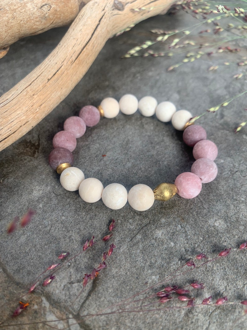 May include: A bracelet made of pink and white beads with gold accents. The bracelet is on a gray textured surface.