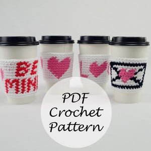 May include: Four crocheted coffee cup cozies in white with pink and black accents. The cozies feature different designs including hearts, the words "Be Mine", and an arrow through a heart. The text "PDF Crochet Pattern" is written in white on a black circle.