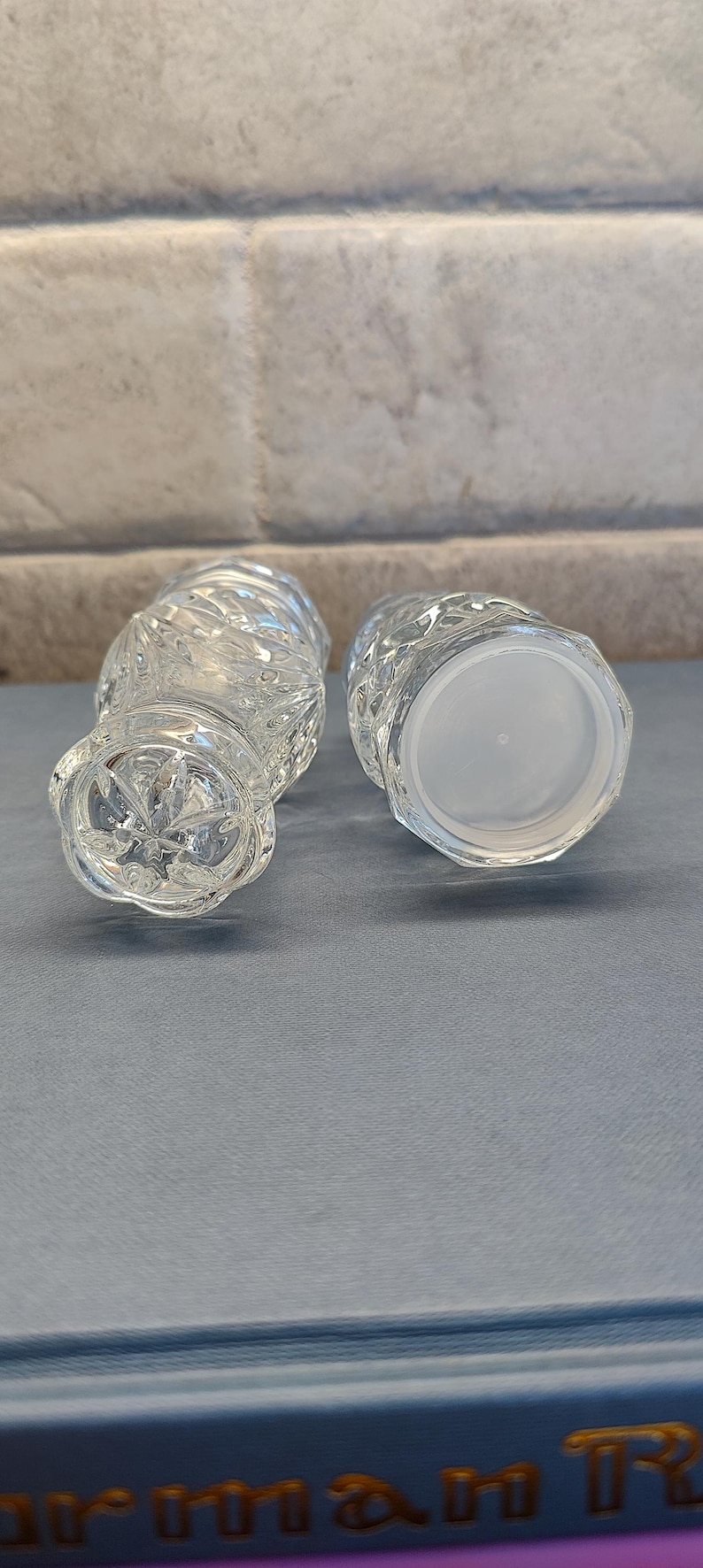 May include: Two clear, cut-glass vases with a textured, diamond-like pattern. One vase is upright, and the other is lying on its side, revealing a white plastic base. The vases are on a blue surface.