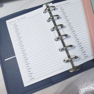 Könnte beinhalten: Eine weiße Seite mit den Worten "BOOKS TO READ" oben. Die Seite ist in zwei Spalten unterteilt, wobei die Wörter "Title" und "Author" mehrmals wiederholt werden. Die Seite ist mit einem silbernen Ringbuchbinder gebunden.