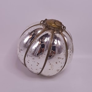 Op de afbeelding: Een zilverkleurig, rond decoratief object met een geribbeld ontwerp. Het object heeft een metallic afwerking met een aangetaste uitstraling en een goudkleurige metalen bovenkant. De algemene vorm lijkt op een pompoen of een decoratieve bal.
