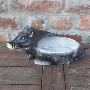 Può includere: Un piatto in ceramica a forma di cinghiale con un interno grigio. Il cinghiale è nero con il muso marrone e le zanne gialle.