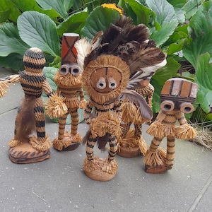 Op de afbeelding: Vier kleine, handgemaakte beeldjes van natuurlijke materialen. Elk beeldje heeft een uniek ontwerp met bruine, zwarte en witte accenten. De beeldjes staan op een grijze betegelde ondergrond.