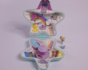 Könnte beinhalten: Ein blaues und violettes, sternförmiges Spielset aus Plastik mit abnehmbarem Deckel. Im Inneren des Spielsets befindet sich ein kleines violettes Schloss mit einem rosafarbenen Dach, ein Regenbogen und eine gelbe Figur. Das Spielset ist geöffnet und der Deckel liegt daneben.