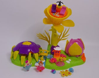 Könnte beinhalten: Ein gelbes Blumenspielset mit einer violetten Blumenbasis, einer Biene oben drauf und zwei Feen. Das Set enthält ein kleines gelbes Haus, eine Brücke und einen Schmetterling.
