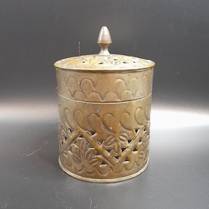 Peut inclure: Un récipient en laiton avec un couvercle, orné d'un motif complexe de feuilles et de volutes. Le récipient est rond et possède un bouton décoratif sur le couvercle.