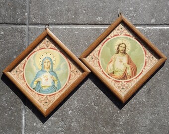 Könnte beinhalten: Zwei gerahmte religiöse Drucke. Einer zeigt eine Figur in blauen Gewändern mit Heiligenschein, der andere eine Figur in roten und weißen Gewändern mit Heiligenschein. Beide sind in rautenförmigen Holzrahmen mit dekorativen Bordüren gefasst.