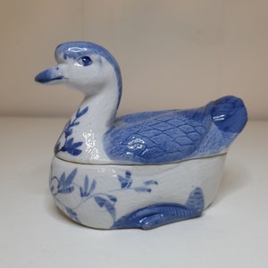 May include: A blue and white porcelain duck figurine with a floral design. The duck is a small trinket box with a hinged lid.