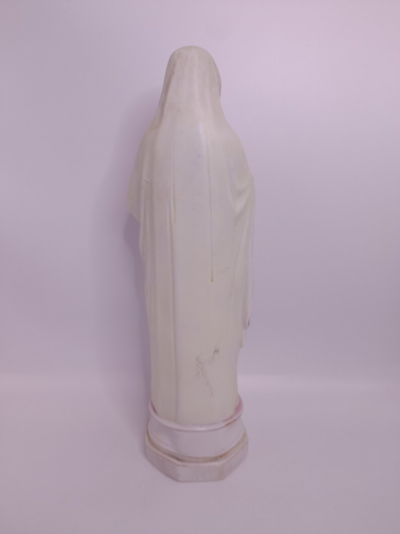 Puede incluir: Estatua de cer&aacute;mica blanca de una mujer con una t&uacute;nica larga. La estatua est&aacute; de pie sobre una base blanca.