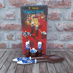 Può includere: Un set da insalata vintage da 5 pezzi. Il set include una scatola con la scritta "5 Piece Salad Set", due cucchiai da insalata in legno e tre contenitori in ceramica con disegni floreali blu. I contenitori sono marroni e bianchi.