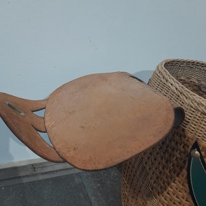 May include: A woven wicker basket with a brown leather strap and handle. The basket has a green and white design on the side.