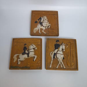 May include: Three wooden plaques with equestrian scenes. Each plaque features a carved relief of a rider on horseback, with text in a foreign language. The riders are dressed in period attire, and the horses are in various poses.