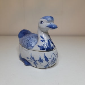 May include: A blue and white porcelain duck figurine with a floral design. The duck is a small trinket box with a hinged lid.