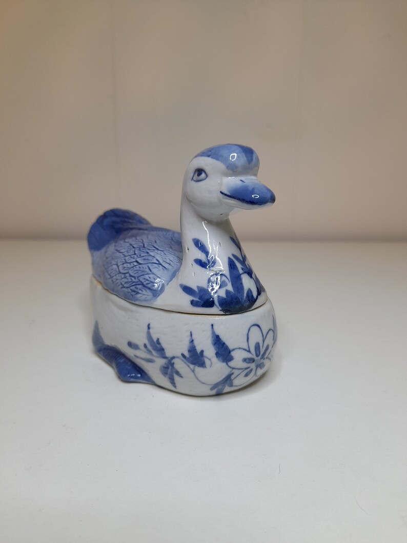 May include: A blue and white porcelain duck figurine with a floral design. The duck is a small trinket box with a hinged lid.