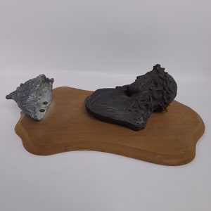 K&ouml;nnte beinhalten: Eine Holzplakette mit einer schwarzen und grauen Skulptur eines M&auml;nnerkopfes mit Dornenkrone. Eine graue und silberne Skulptur einer Muschel befindet sich ebenfalls auf der Plakette.