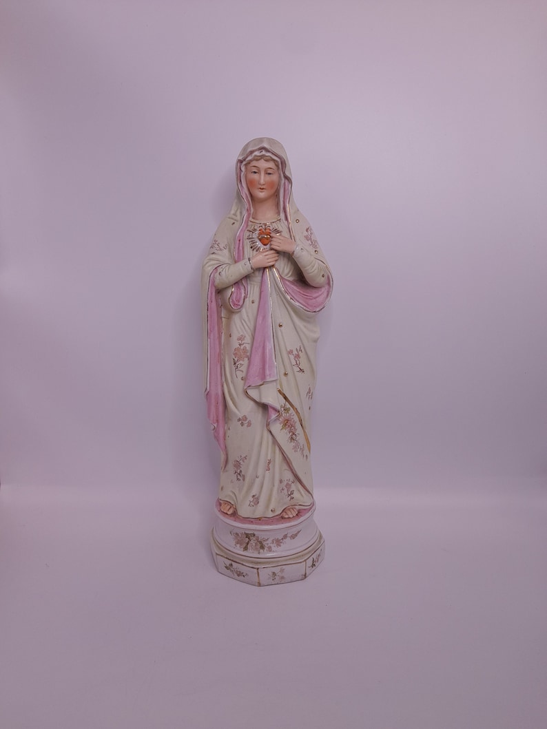 Puede incluir: Una estatua de porcelana de la Virgen Mar&iacute;a con una t&uacute;nica rosa y blanca y un dise&ntilde;o floral. Ella sostiene un coraz&oacute;n en sus manos.