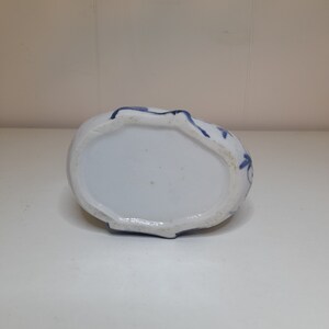 May include: The bottom of a white ceramic vase with blue floral designs. The vase has a rounded shape and a slightly raised rim.