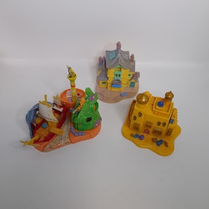 Op de afbeelding: Drie kleurrijke miniatuur speelsets. Eén is een geel en oranje piratenschip, een ander is een geel huis met een grijs dak en de derde is een geel kasteel met blauwe koepels. Dit speelgoed komt waarschijnlijk uit de jaren 1990.
