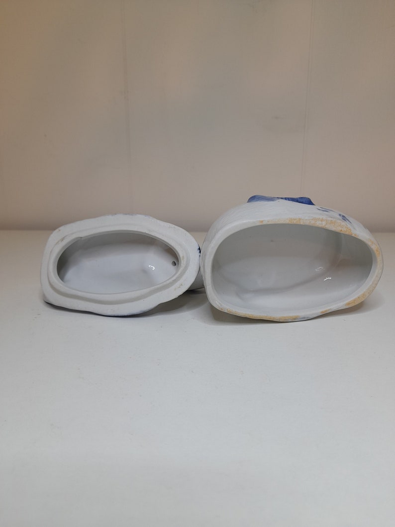 May include: Two white ceramic containers with blue and white floral designs. The containers are open and empty, revealing the white interior.