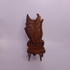 May include: A carved wooden seashell sculpture with intricate details. The sculpture is a rich brown color and is mounted on a small wooden stand with brass legs. The seashell design features detailed carvings.