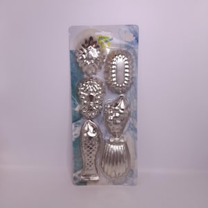 May include: A set of six silver-colored metal cookie cutters in various shapes, including a fish, seashell, and floral designs. The cutters are packaged on a blue and white patterned backing.