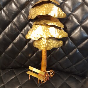 May include: A gold metal sculpture of a tree with a bench and a bicycle underneath. The tree has a textured surface and the sculpture is signed "Bruce Lu 2013".