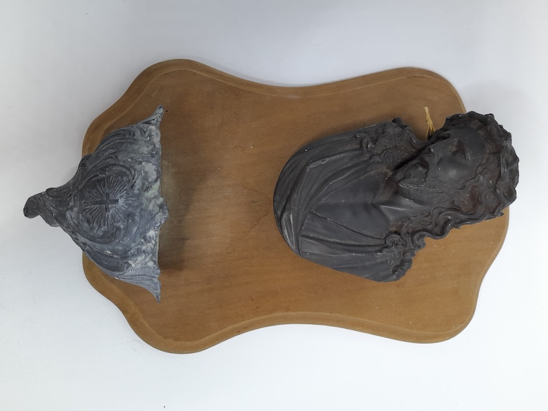 K&ouml;nnte beinhalten: Eine Holztafel mit zwei daran befestigten schwarzen Gipsfiguren. Eine Figur ist eine B&uuml;ste einer Person mit langen Haaren, die andere ist ein dekoratives St&uuml;ck.