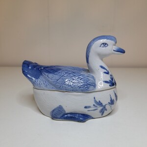 May include: A blue and white porcelain duck figurine with a lid. The duck has a detailed design and is a decorative piece.