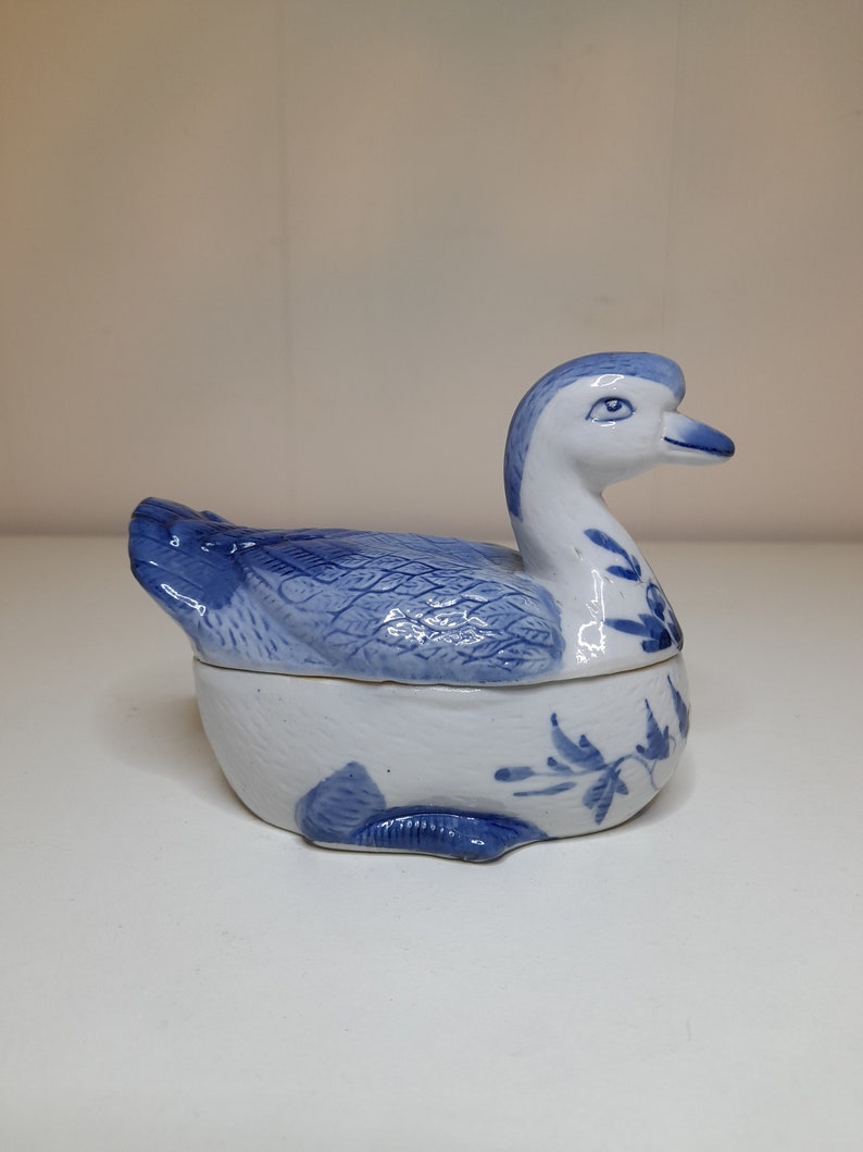 May include: A blue and white porcelain duck figurine with a lid. The duck has a detailed design and is a decorative piece.