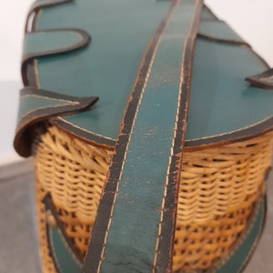 May include: A vintage wicker basket with a teal leather lid and a long teal leather strap. The basket is woven with a light brown wicker.