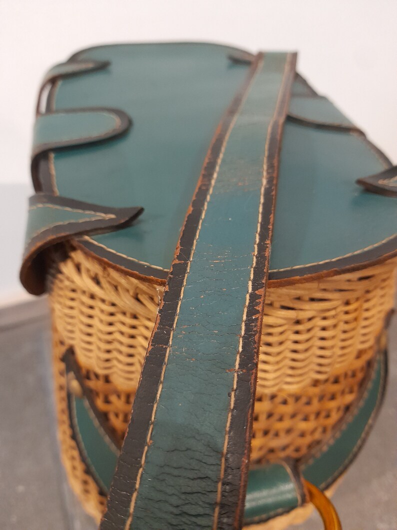 May include: A vintage wicker basket with a teal leather lid and a long teal leather strap. The basket is woven with a light brown wicker.