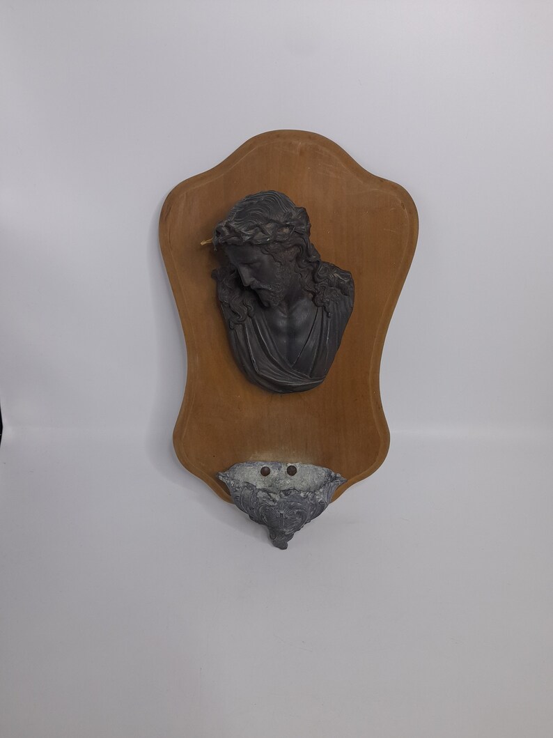 K&ouml;nnte beinhalten: Eine Holztafel mit einer Reliefb&uuml;ste von Jesus, der eine Dornenkrone tr&auml;gt. Die Tafel hat unten einen kleinen, grauen, muschelf&ouml;rmigen Beh&auml;lter.