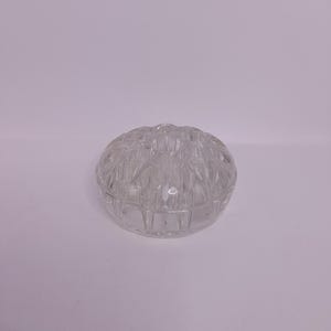 May include: A clear, spherical glass flower frog with a textured, geometric design. The frog is designed to hold flowers in place and is a decorative addition to any vase or floral arrangement.